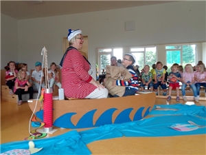 Frau sitzt mit Kind in einem Pappboot und spielt anderen Kindern ein Theaterstück vor