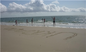 Personen schwimmen im Meer in strandnähe, im Sand steht "Ukraine" geschrieben