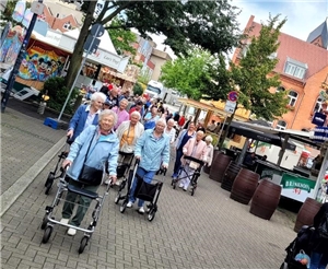 Eine Gruppe Seniorinnen mit Rollatoren läuft durch die Innenstadt mit Kirmesbuden.