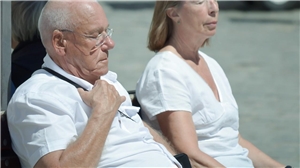 Ein älterer Mann und eine ältere Frau sitzen im Sonnenschein auf einer Parkbank.