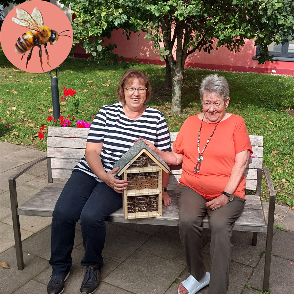 Schäfer und Löhr sitzen auf einer Bank im Garten, zwischen ihnen das Bienenhotel