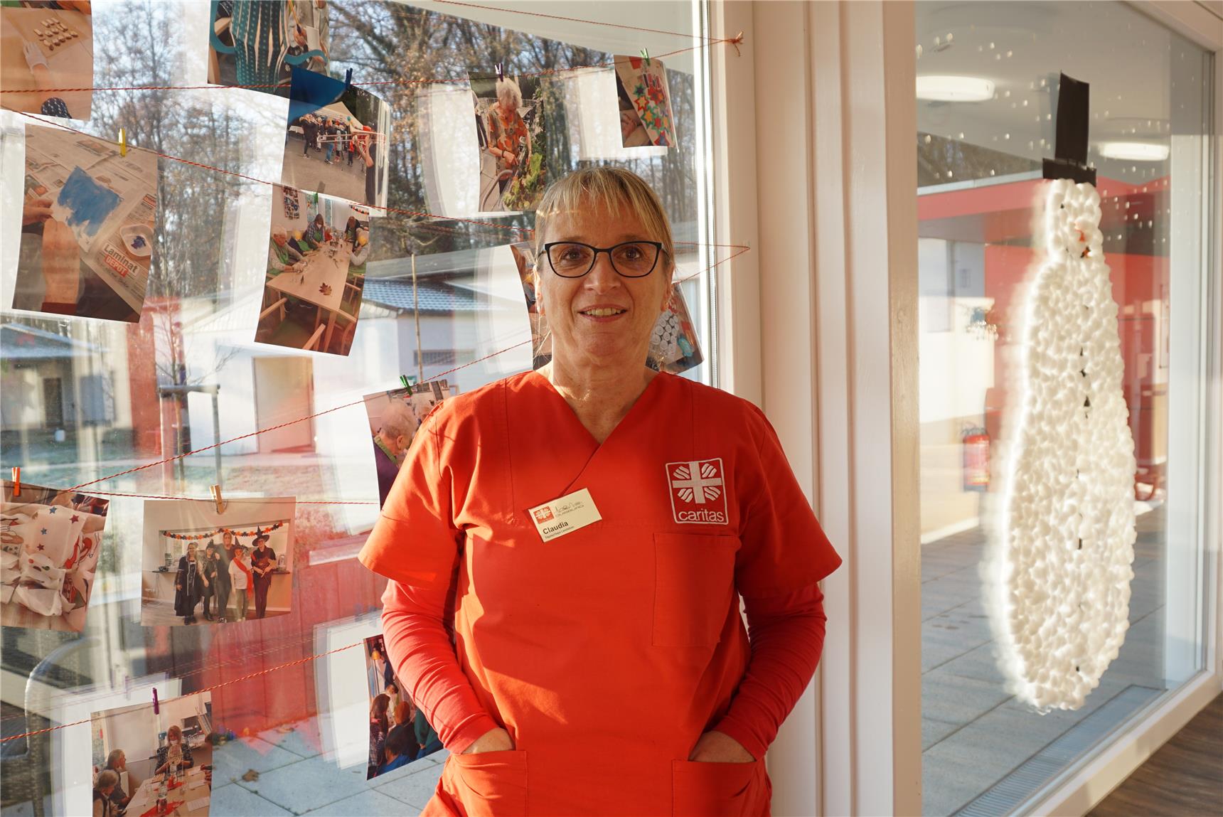 Claudia Seifert steht vor einer Fensterfront, die mit bunten Fotos und einem großen Schneemann aus Watte dekoriert ist
