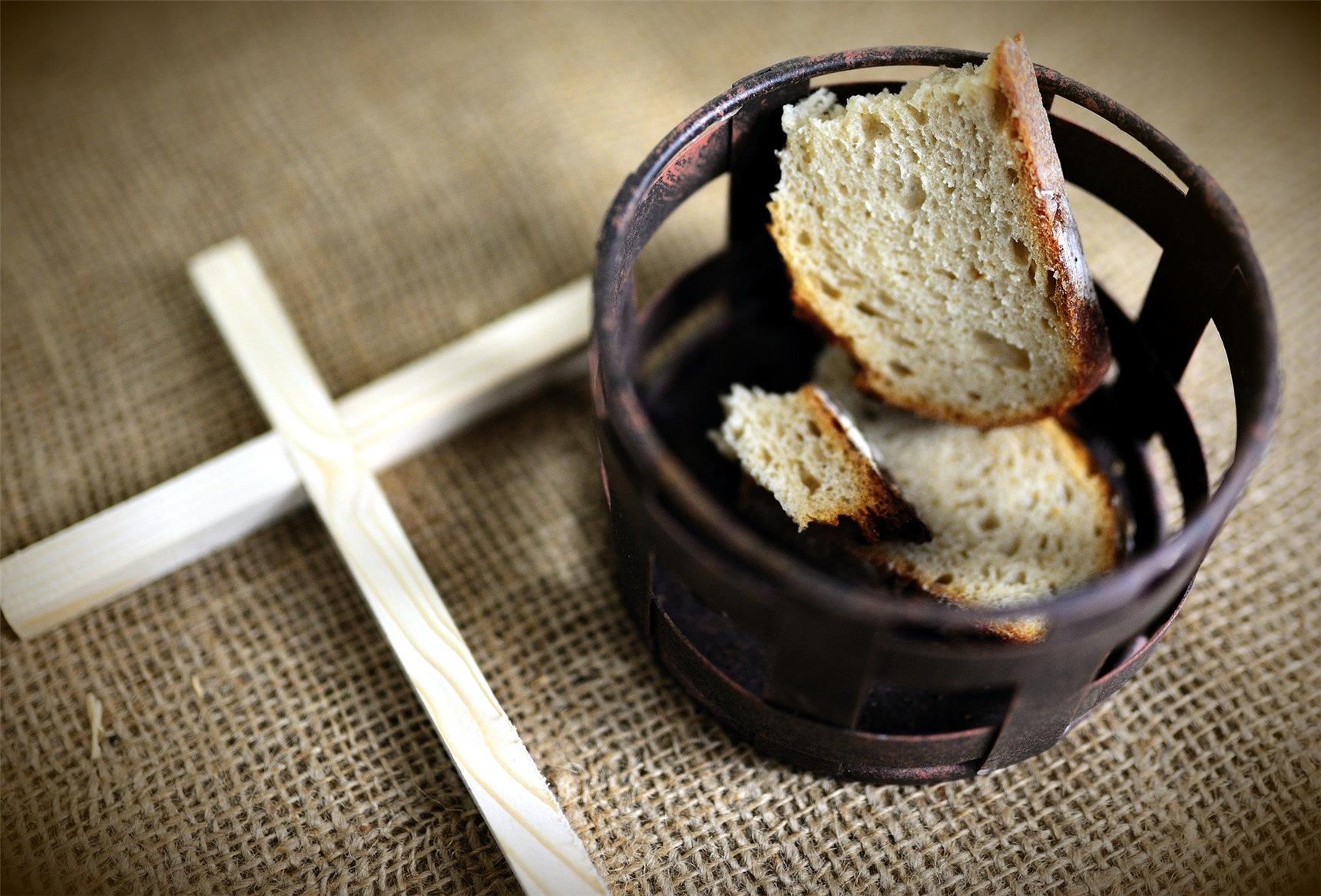 Neben einer Schale mit Brotstücken liegt ein dünnes Holzkreuz.