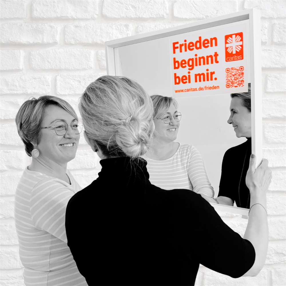 Sandra und Katharina stehen vorm Spiegel mit aufgeklebtem Motto und lächeln