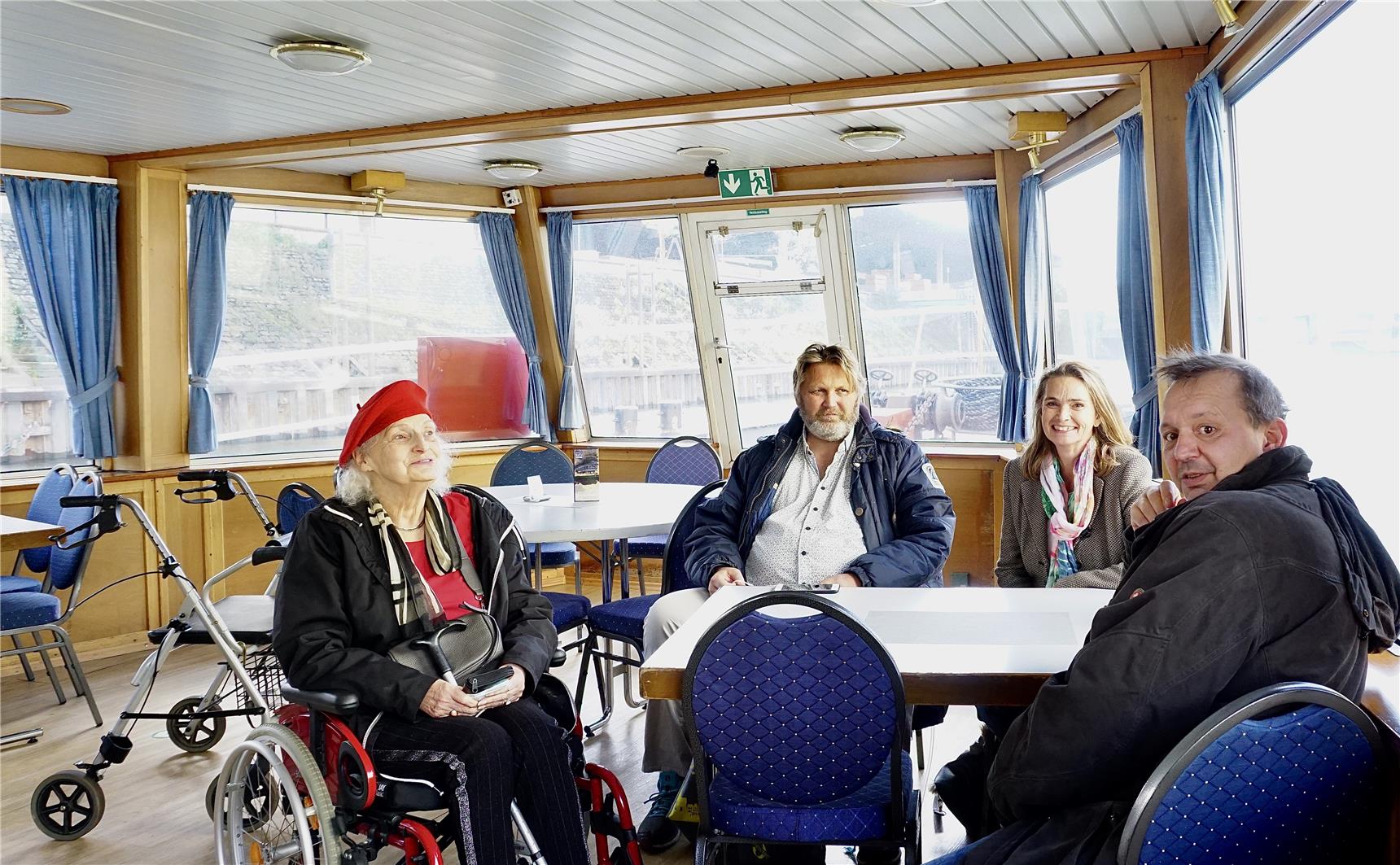 Die beiden Bewohner, die Bewohnerin und ihre Betreuerin sitzen im Bug des Schiffes vor der Fensterfront gemeinsam an einem Tisch