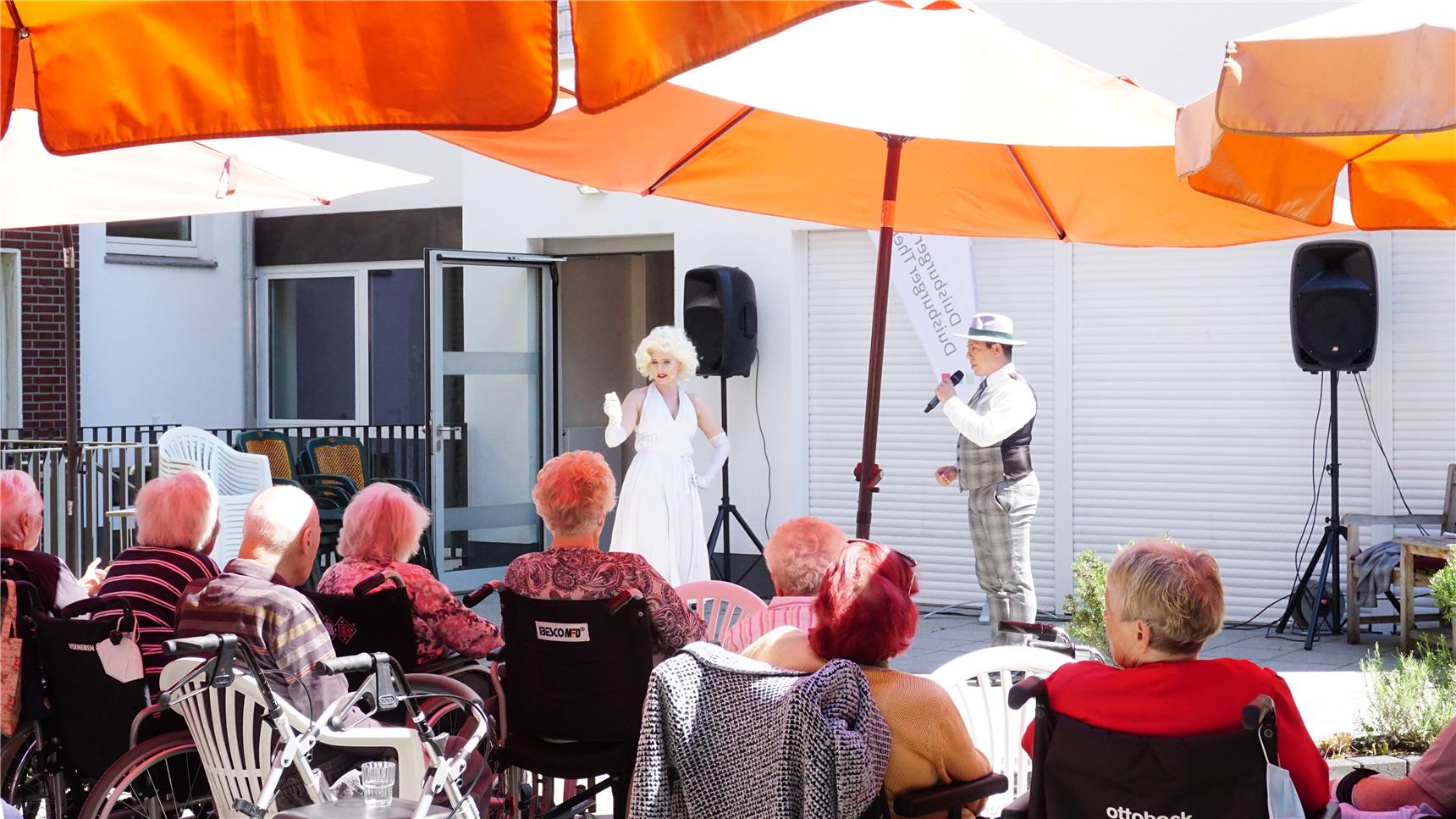 Sängerin als Marilyn Monroe und Sänger als Frank Sinatra stehen von den Senior*innen im Innenhof des Altenheims