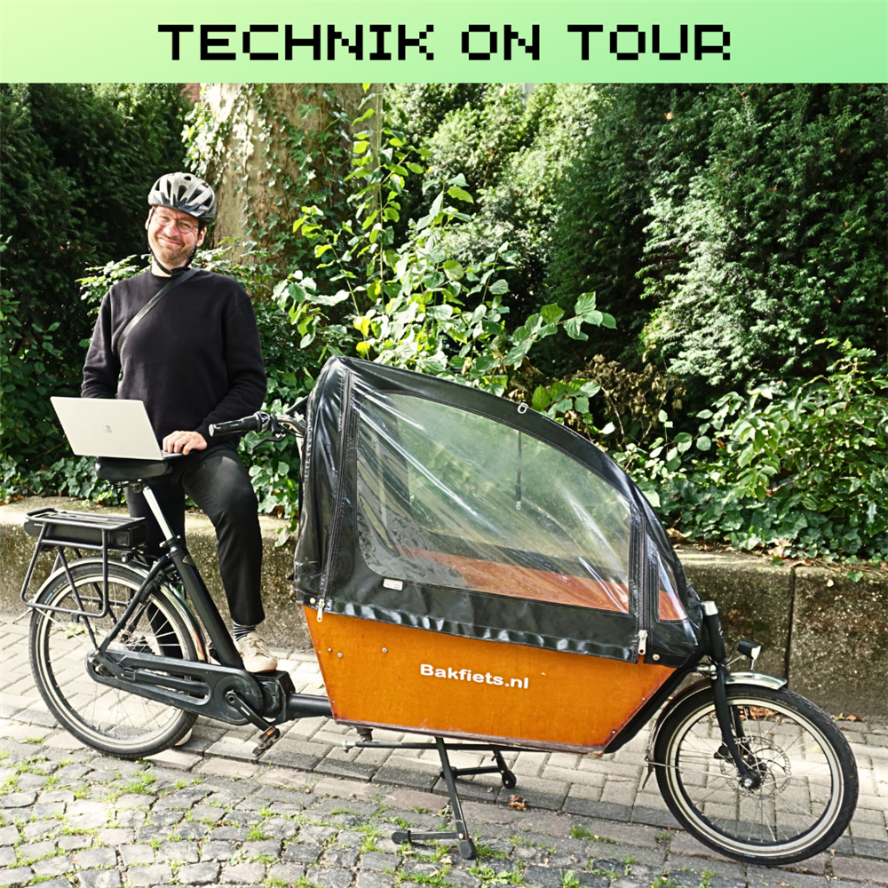 Bartosz steht mit Laptop neben seinem Lastenrad