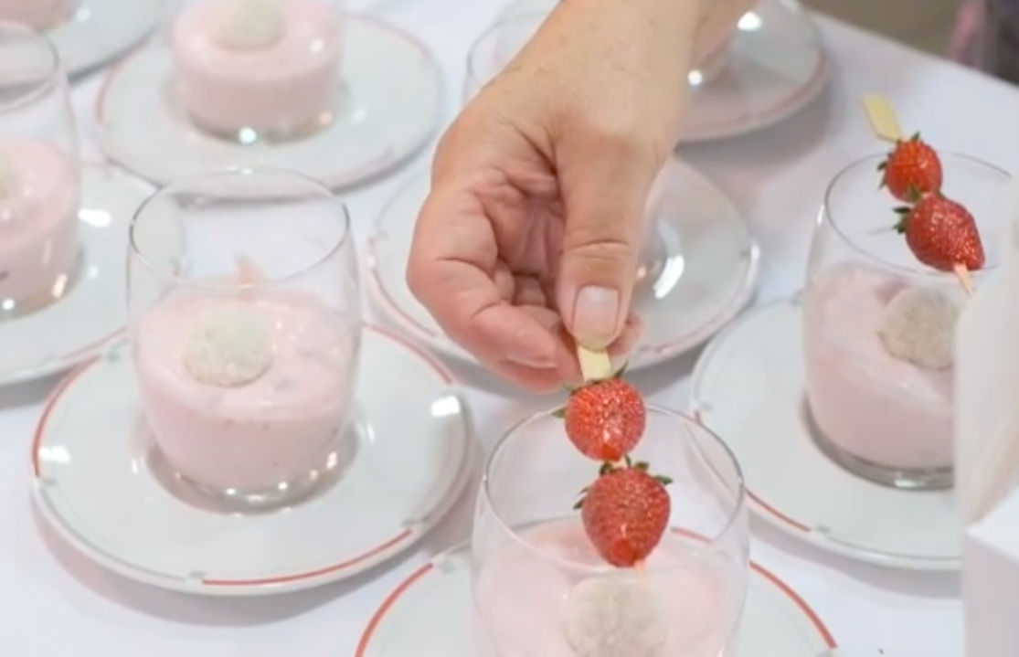 Zahlreiche Dessergläser mit Kokoscreme, eine Hand legt einen Erdbeerspieß darauf