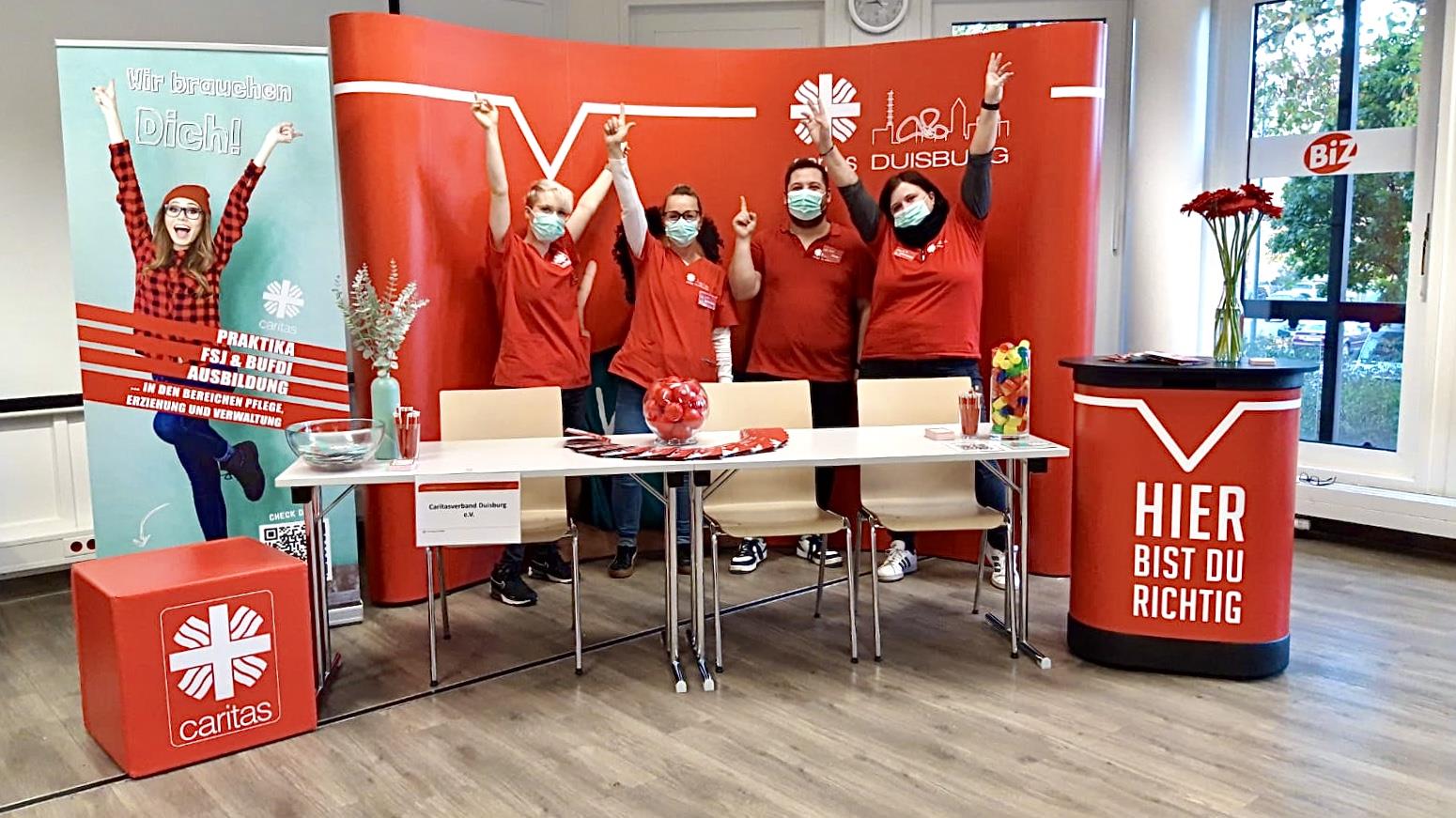 Das Team mit drei Frauen und einem Mann steht im rot-weißen Messe-Stand 