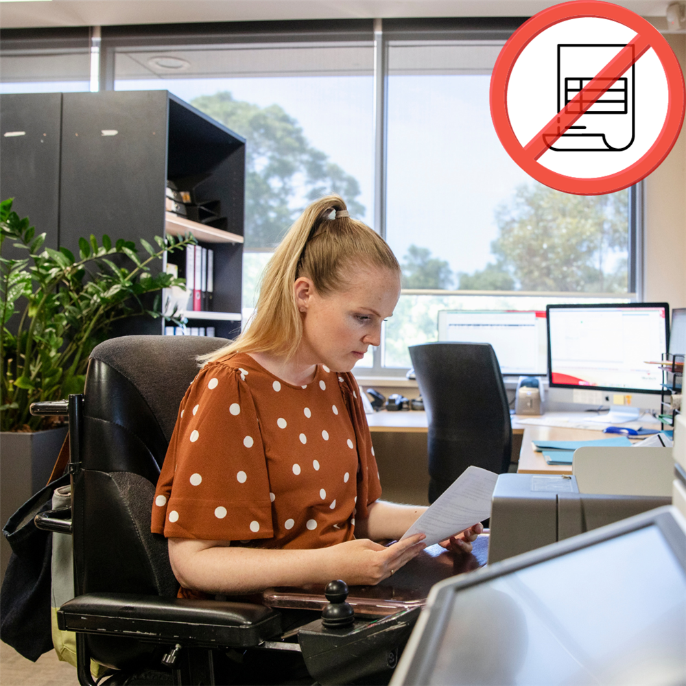 Mitarbeiterin am PC-Arbeitsplatz mit Dokument in der Hand