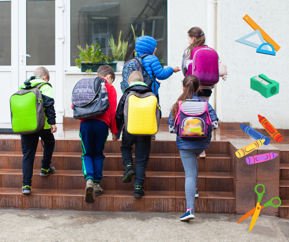 Sechs Kinder, von hinten zu sehen, gehen die Stufen zum Schulgebäude hoch