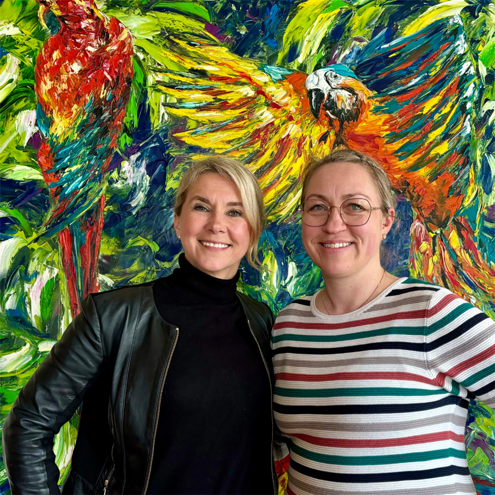 Katharina und Sandra stehen lächelnd vor buntem Hintergrund