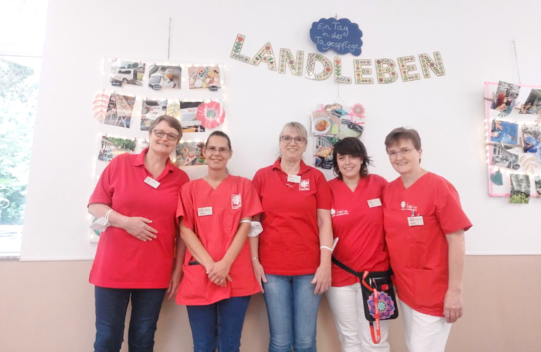 Fünf Mitarbeiterinnen stehen vor einer bunten Bilderwand und strahlen in die Kamera