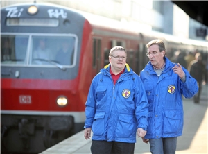 Zwei Herren am Bahnsteig vor einem Zug in der Bekleidung der Bahnhofsmission