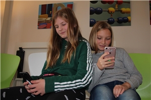 Zwei Mädchen sitzen nebeneinander und blicken auf ihre Handys