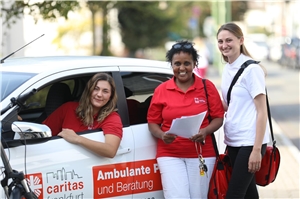 Drei Frauen in und vor einem Auto der ambulanten Pflegestation der Caritas