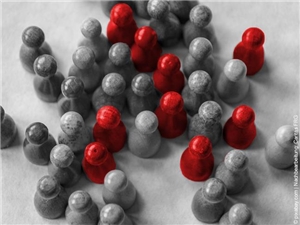 Bildtotale von schräg oben: Einfache Spielfiguren aus Holz arrangiert. In Graustufen. Neun in Rot hervorgehoben. (c) pixabay.com|Nachbearbeitung: Caritas FRG.