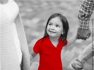 Kindergartenmädchen läuft glücklich an der Hand zwischen seinen Eltern. In Graustufen, rote Illustration des T-Shirts. (c) Yakobchuk Olena | www.stock.adobe.com | Nachbearbeitet Caritas FRG.