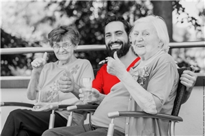 Pfleger sitzt zwischen zwei Seniorinnen auf der Terrasse im Seniorenheim. In Graustufen, Shirt des Pflegers rot illustriert. (c) Kzenon|www.stock.adob.com|Nachbearbeitet direttissima. at