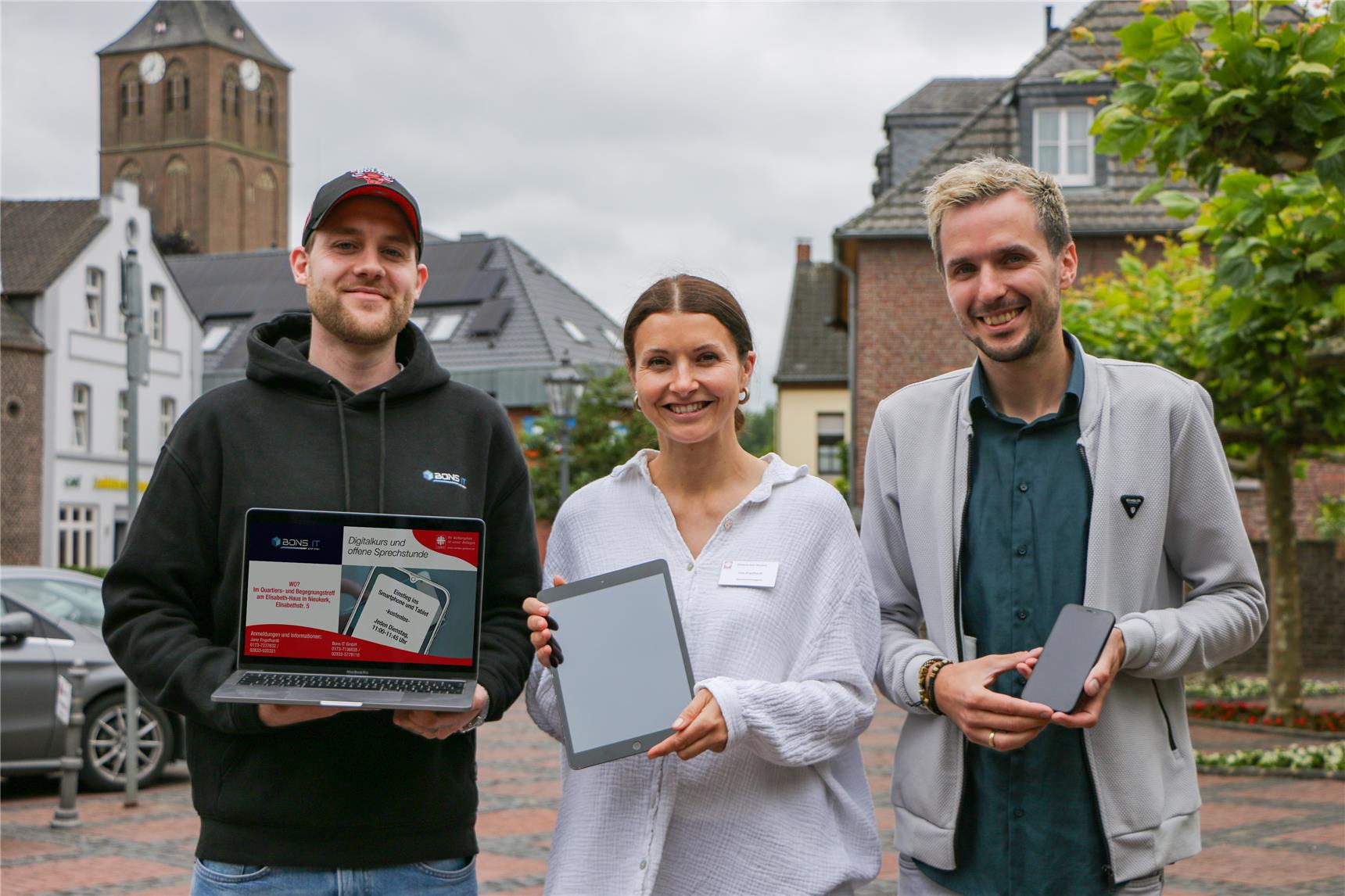 Jane Engelhardt steht mit einem Tablet in der Hand zwischen sowie Patrick Bons (frechts), der ein Smartphone in die Kamera hält und Niclas Habrich (links) mit Laptop.