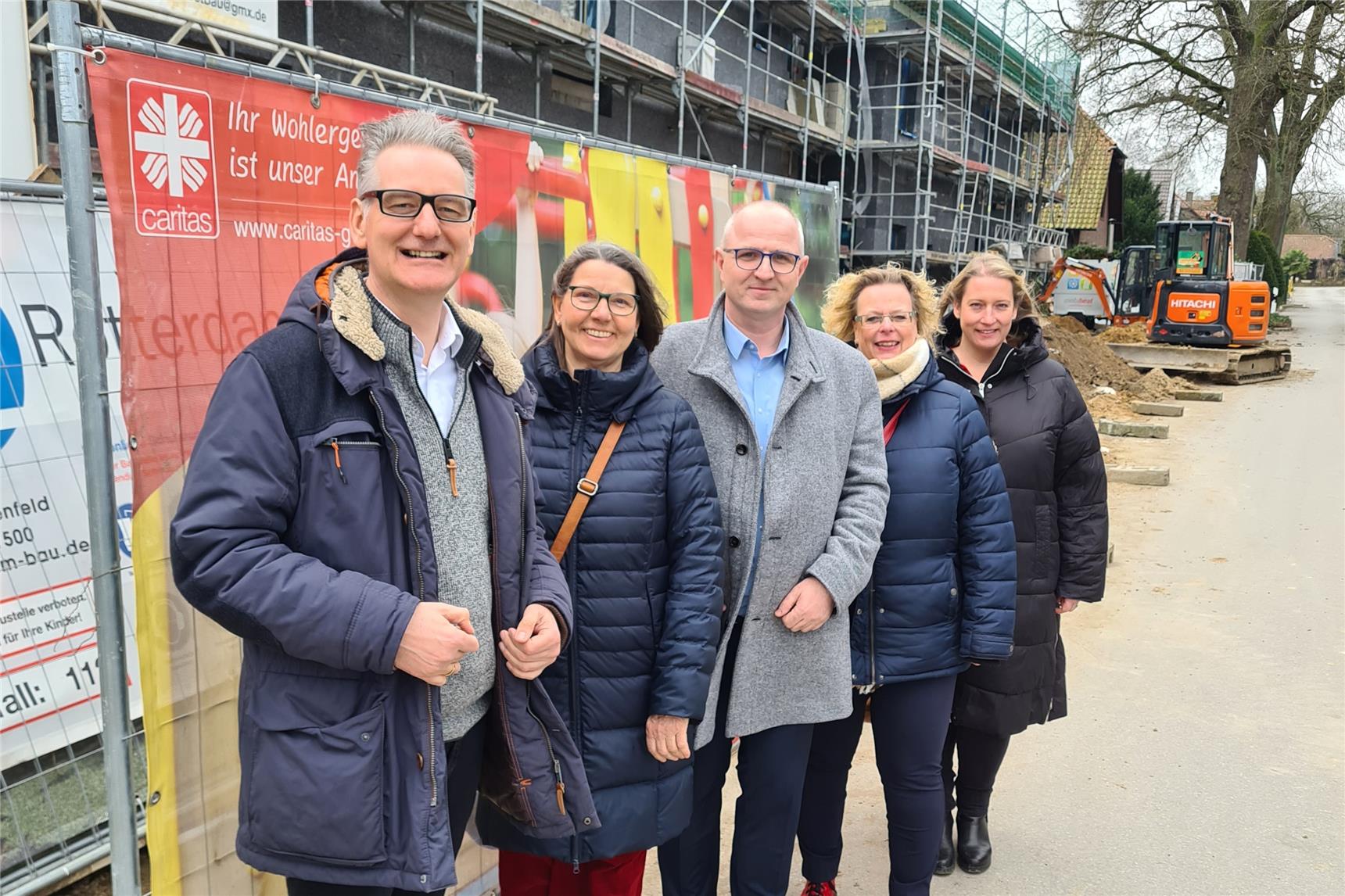 Fünf Personen stehen nebeneinander vor einem Bauzaun an einer Baustelle der Caritas