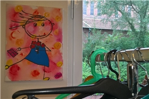 Kleiderstube Logo Gemaltes Bild von einem Mädchen mit Blumen, Kleiderbügel hängen im Vordergrund