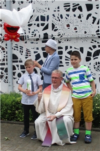 Kommunion Haus St. Rafael Drei Kommunionkunder und ein Pfarrer posieren für ein Gruppenbild