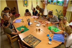 Besucherinnen und Besucher der Tagesstätte malen Um einen Tisch sitzen Besucher der Tagesstätte und malen