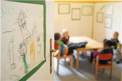 KinderHaus innen Gesprächskreis Betrachter sieht eine angelehnte Tür, im Nebenzimmer sitzen Kinder an einem Tisch