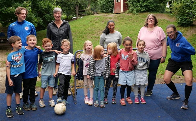Kinder und Erwachsene auf blauem Flies vor einem kleinen Fußballtor. 
