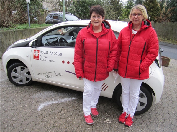 Zwei Frauen in roten Jacken vor einem Caritas-Fahrzeug