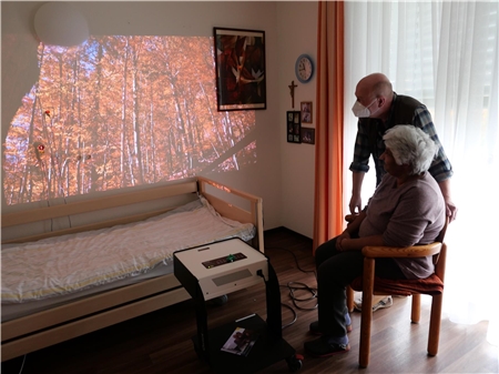 Eine alte Frau schaut auf ein Bild mit Bäumen, das an die Wand projiziert wurde.