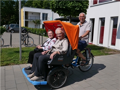 Ein Mann fährt zwei alte Frauen in einer Rikscha. 