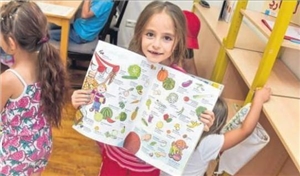 Mädchen zeigt ein Bilderbuch mit Abbildungen verschiedener Gemüsesorten in zwei Sprachen