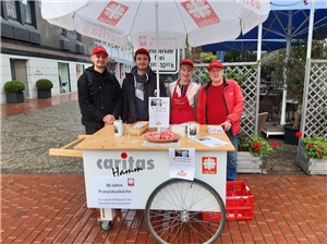 Vier Personen stehen zum Portrait mit einem Rollwagen der Caritas Hamm und verkaufen Brot