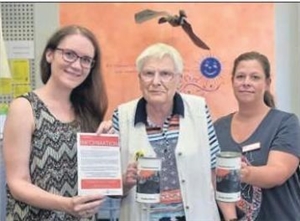 Seniorin und zwei Frauen zeigen ein Plakat und Spendendosen