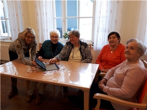 Vier Frauen sitzen am Tisch, eine Frau zeigt ihnen die Funktion eines Tablets