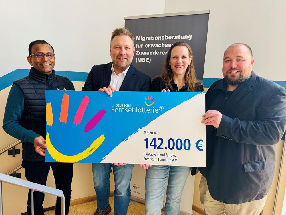 vier Personen bei der Scheckübergabe der Deutschen Fernsehlotterie halten den symbolischen Scheck