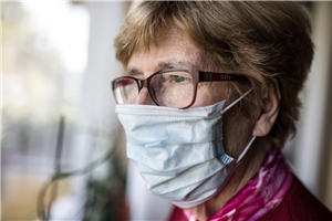 Seniorin mit Mund-Nase-Schutz schaut aus dem Fenster