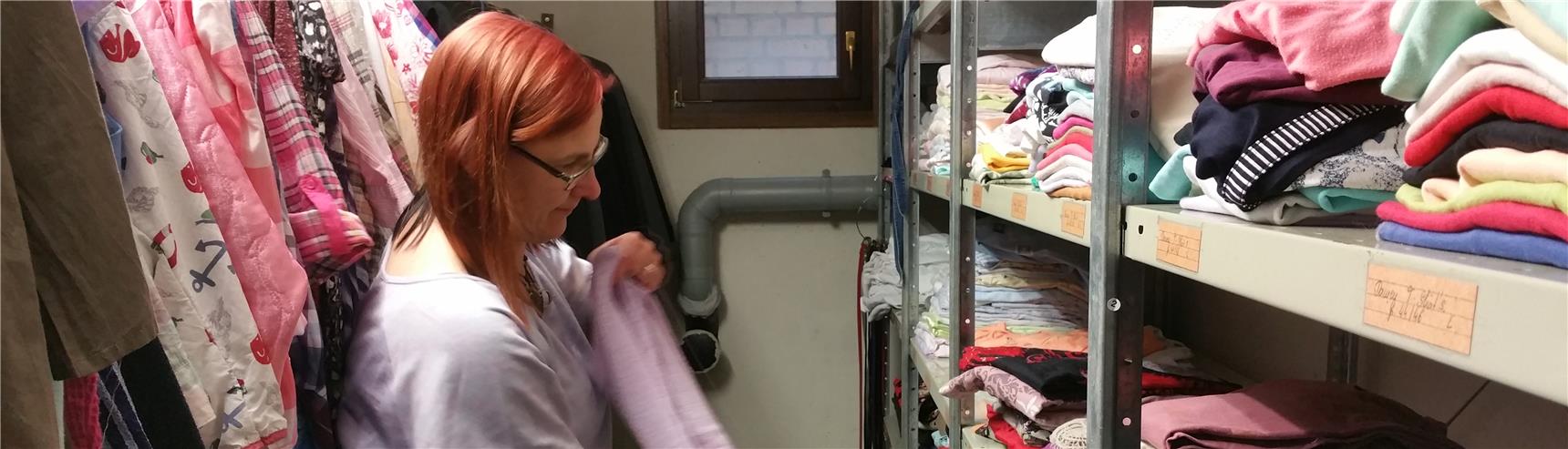 eine ehrenamtliche legt ein Stück Kleidug zusammen und steht dabei im Gang der Kleiderkammer