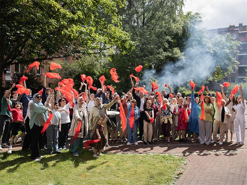 Große Gruppe von Menschen in einem Garten winkt mit roten Tüchern