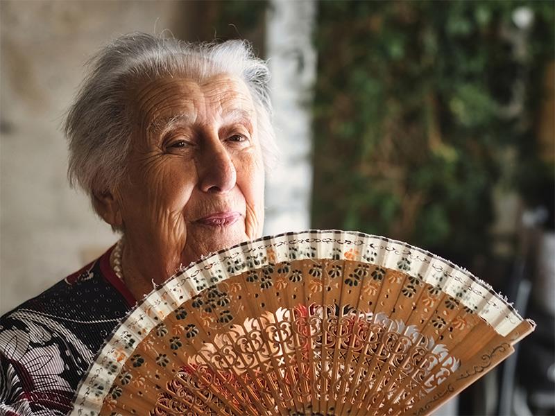 lächelnde alte Dame fächelt sich mit einem Fächer Luft zu