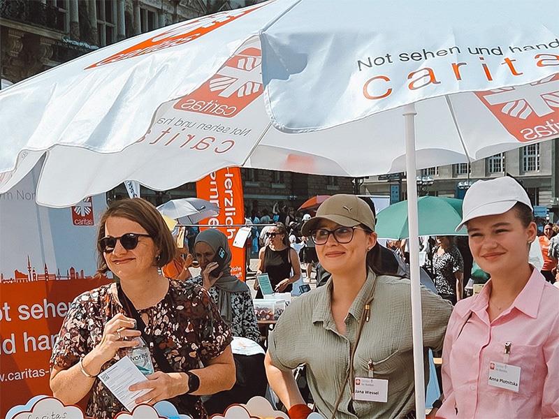 Drei Caritasmitarbeiterinnen an einem Infostand