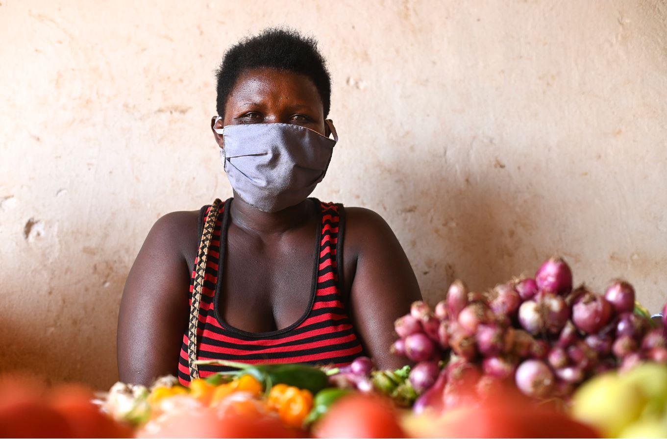 Frau mit Maske an einem Gemüsestand