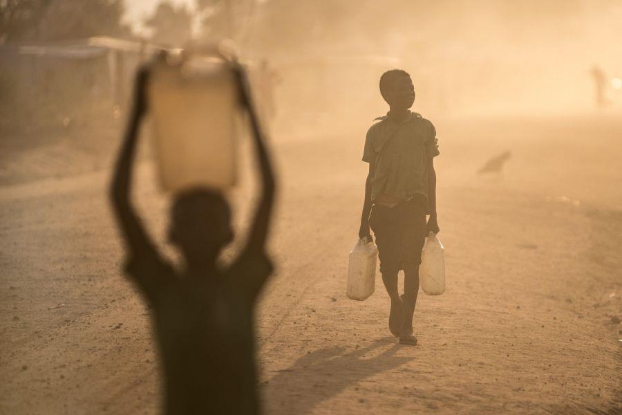 2 Jungen auf einer staubigen Straße - einen Wasserkanister tragend