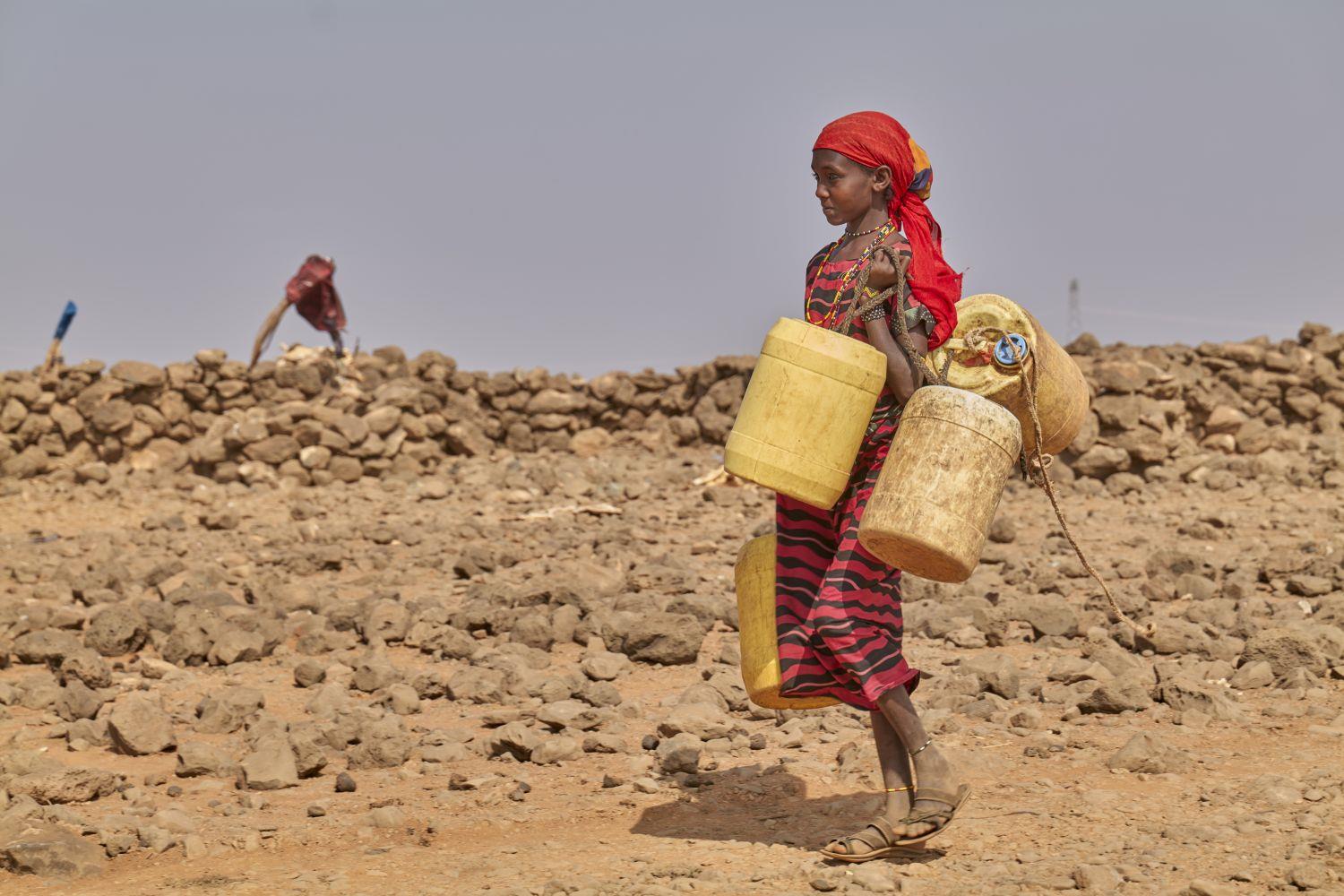 Mädchen in Kenia trägt Wasserkanister durch trockene Landschaft. Ein Symbol für den Wassernotstand in Afrika – ohne Zugang zu einem nahen Brunnen.