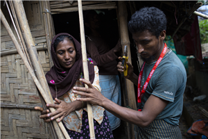 Ein Caritas-Mitarbeiter hilft Toyaba_Khatun dabei, eine Wand ihrer Hütte auszubessern