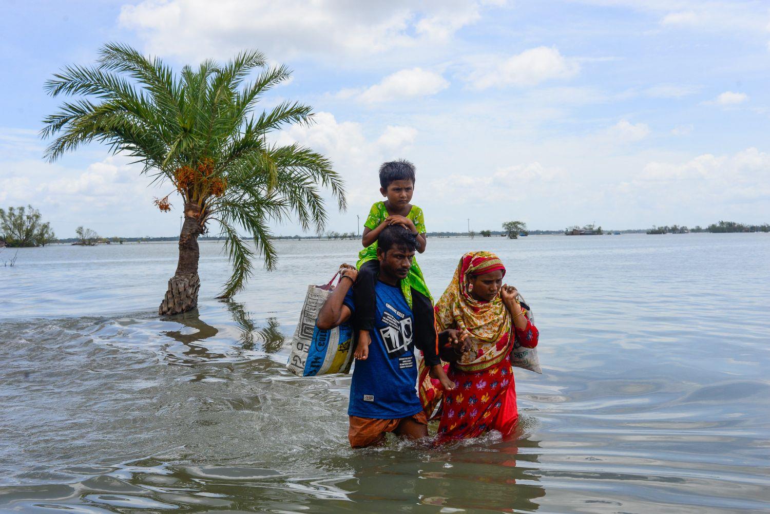 Eine Familie in Bangladesch wartet durchs Wasser. Infolge eines Zyklons wurde alles überflutet - sie haben ihr Haus verloren.