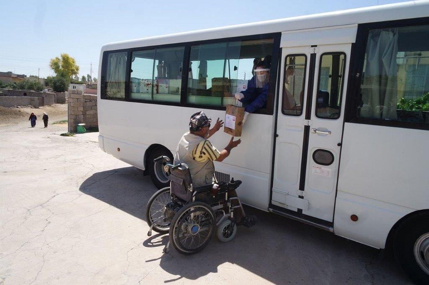 Ein Mann in einem Rollstuhl erhält ein Hygienekit von einer Mitarbeiterin der Caritas Irak.