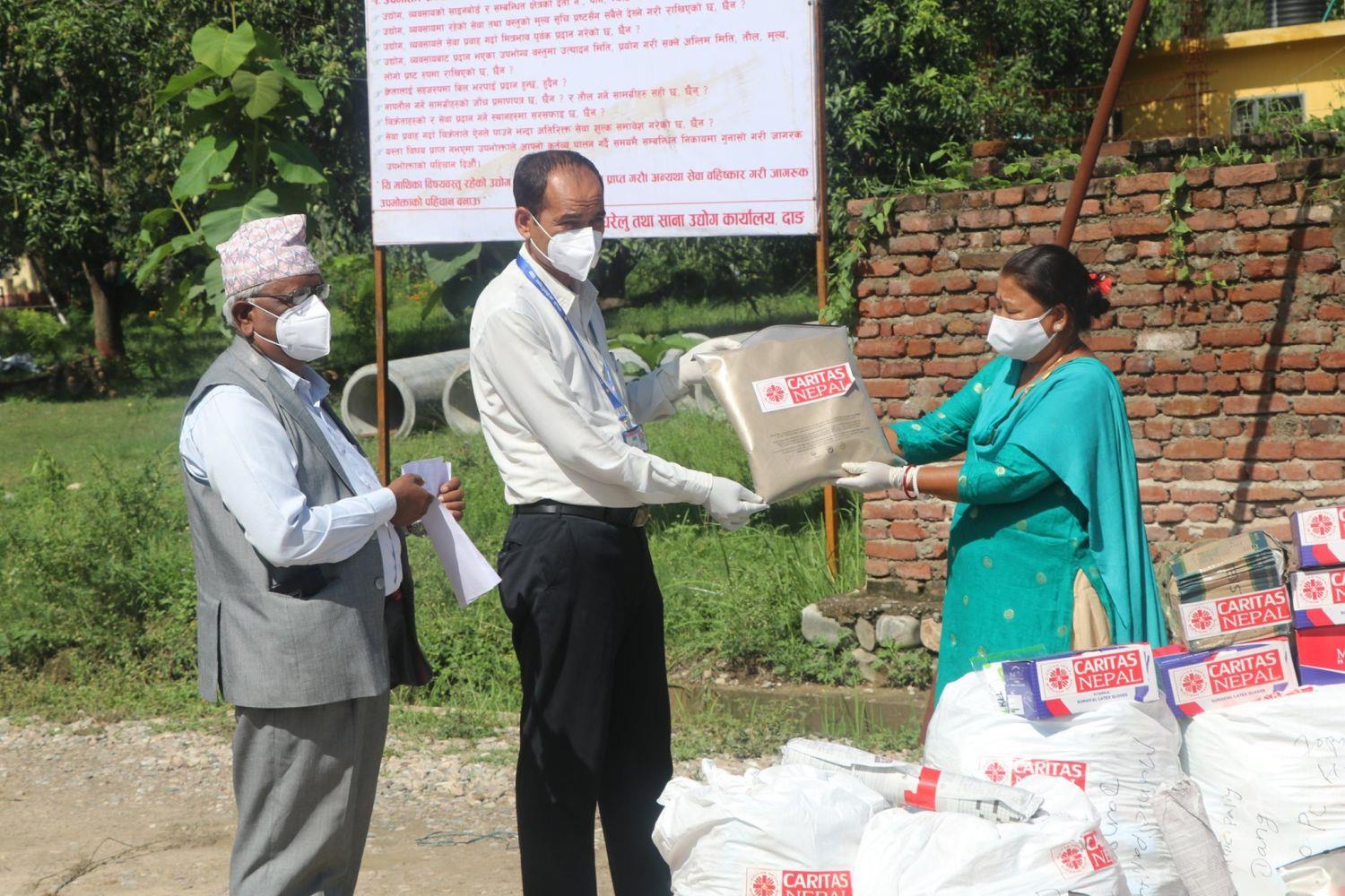 Eine Caritas Mitarbeiter verteilt ein Paket mit Saatgut an eine Nepalesin.
